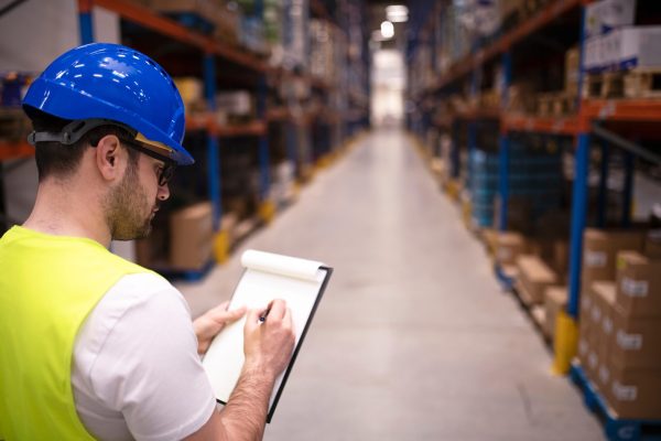 Factory worker holding clipboard and checking inventory of warehouse storage department.